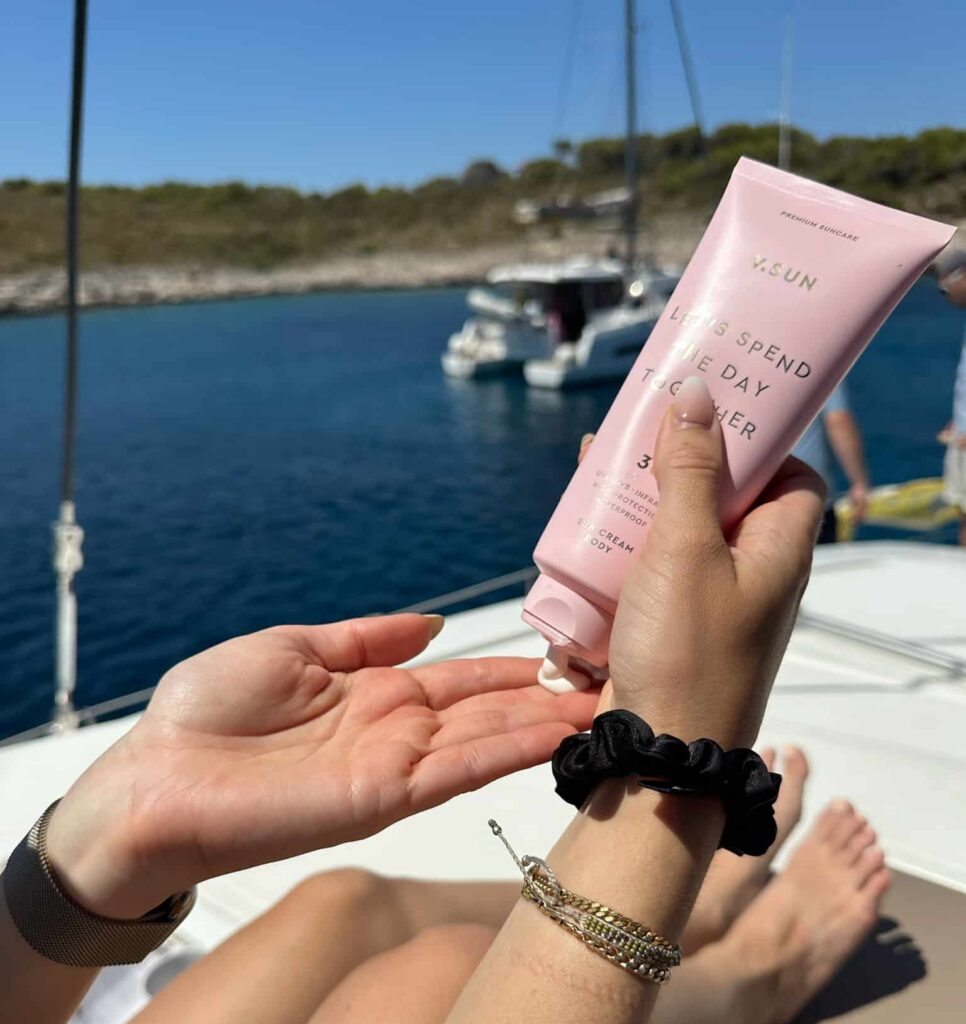 Sonnencreme auf Katamaran mit Segelboot im Hintergrund beim Segeltörn Kroatien sailwithus