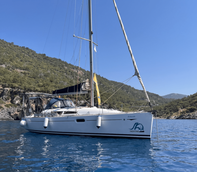 A white sailwithus yacht lying at anchor in a calm, clear bay