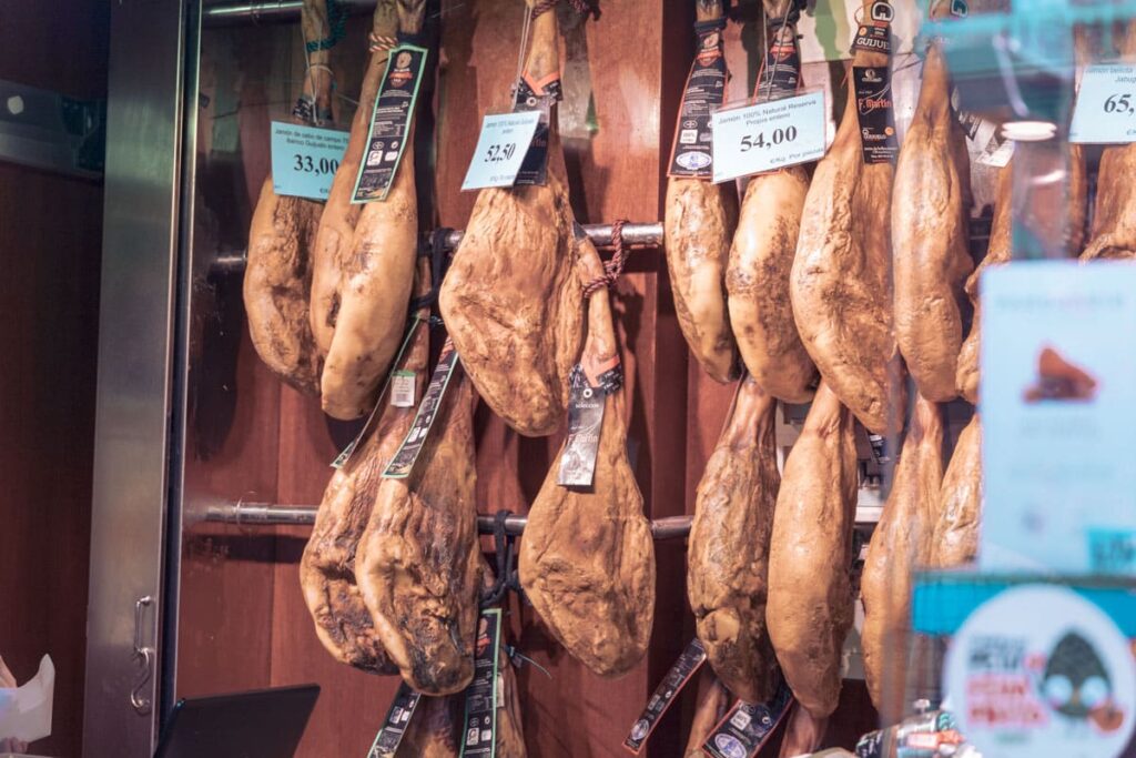 Aufgehängte Serrano-Schinkenkeulen im Marktstand von Palma de Mallorca mit Preisschildern – segeln spanien sailwithus