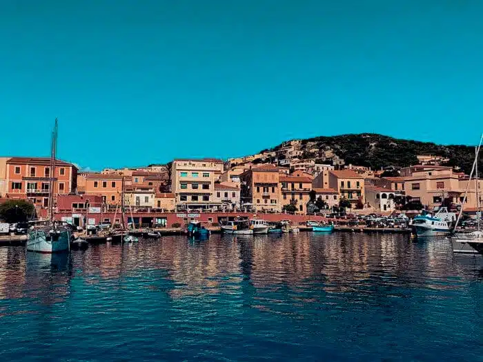 A colourful Sardinian harbour town with a catamaran anchored in calm turquoise water