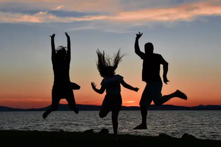 Silhouette drei springender Freunde beim Sonnenuntergang am Meer – segeltörn junge leute sailwithus
