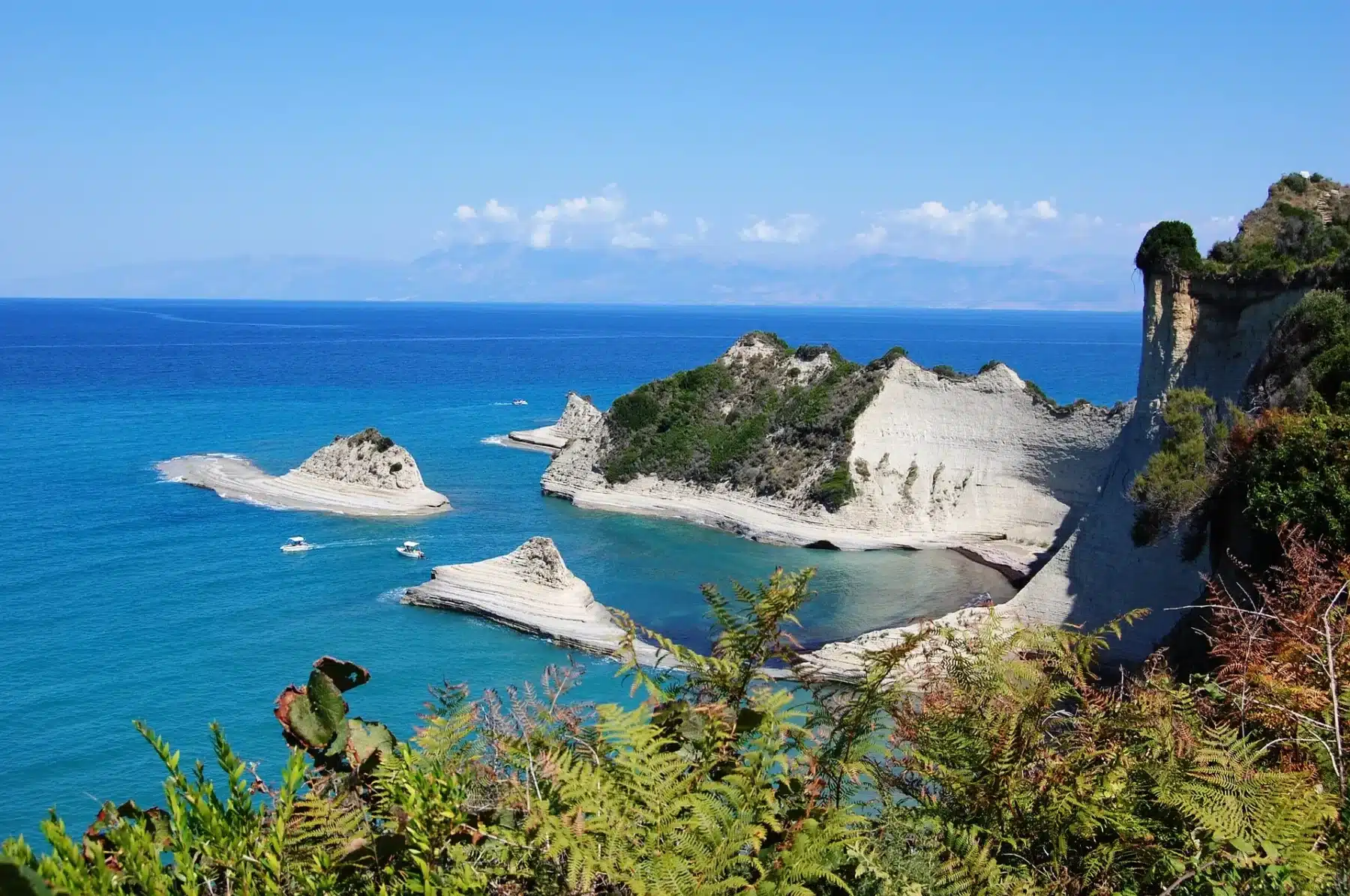The green coastline of Corfu with clear turquoise water and a sailing yacht