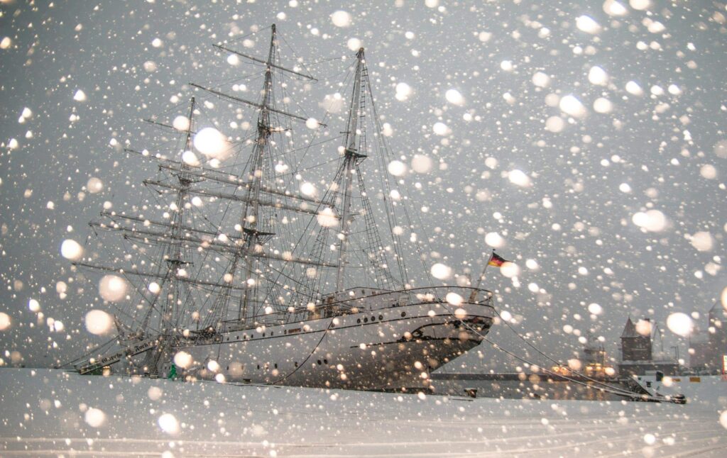 Sailing ship docked in snowy Stralsund harbor, Germany, during winter snowfall.